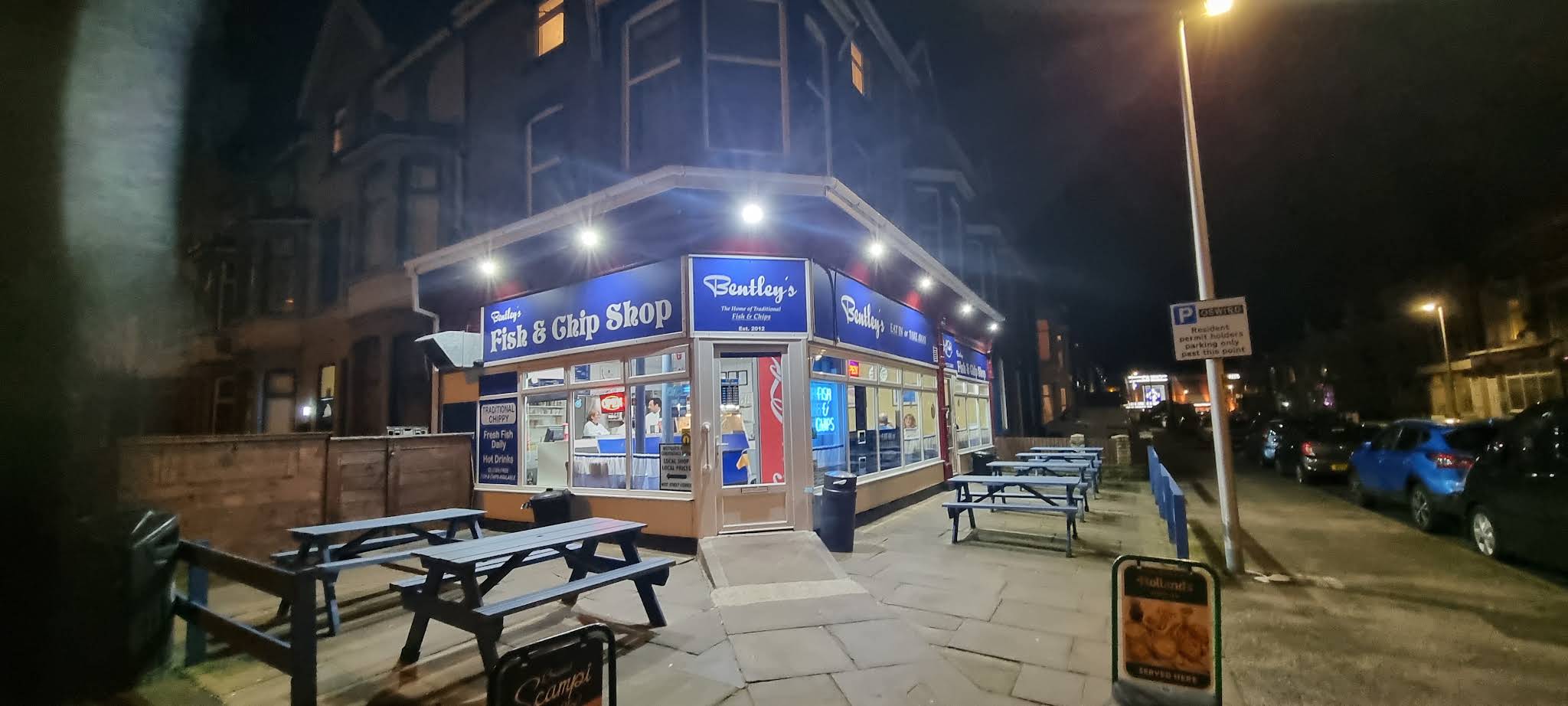 Bentley’s complete corner shopfront at night, with its blue signs, entrance and threshold visible.